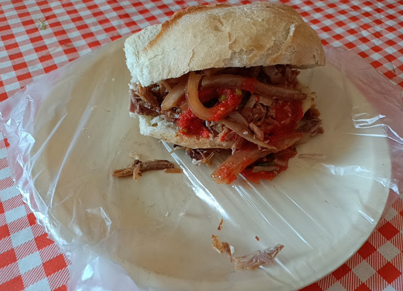 Torta de carnitas servida en plato blanco con salsa roja